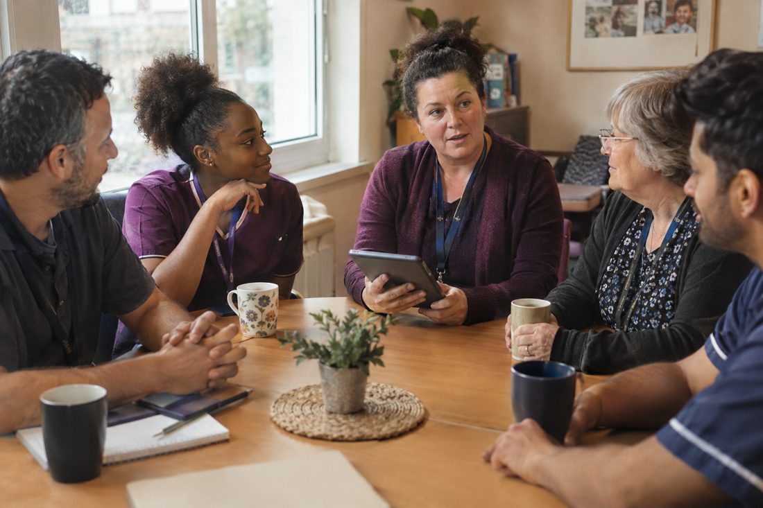 A health and care team in a morning huddle, a manager holding a tablet