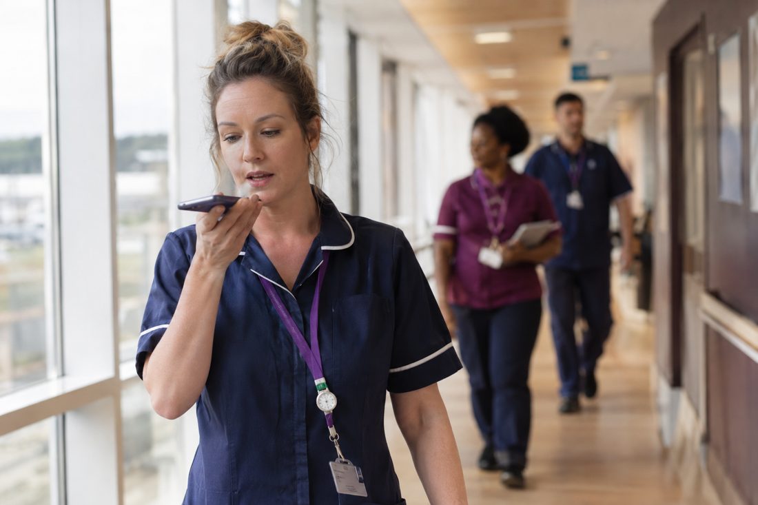 A team leader recording a voice note on her phone while walking along a corridor